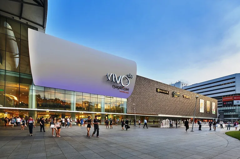 The main entrance of VivoCity at HarbourFront in early-evening light, with shoppers crossing the forecourt beside the fountains